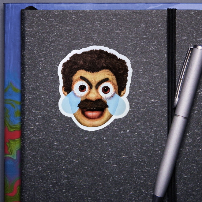 Kiszkiloszki sticker slapped on a gray notebook. A head of the AAAaaa Guy from Kiszkiloszki animation. The man is screaming in a mix of anger and sadness, with an open mouth and comic-like blue tears streaming from his wide open brown eyes.
