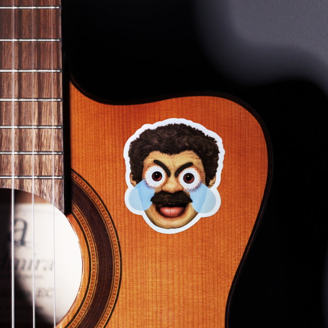 Kiszkiloszki sticker slapped on a front of a guitar. A head of the AAAaaa Guy from Kiszkiloszki animation. The man is screaming in a mix of anger and sadness, with an open mouth and comic-like blue tears streaming from his wide open brown eyes.