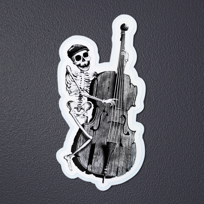 Kiszkiloszki sticker laying on a gray background. A happy skeleton jazzman in a cap is playing on an old, broken double bass.