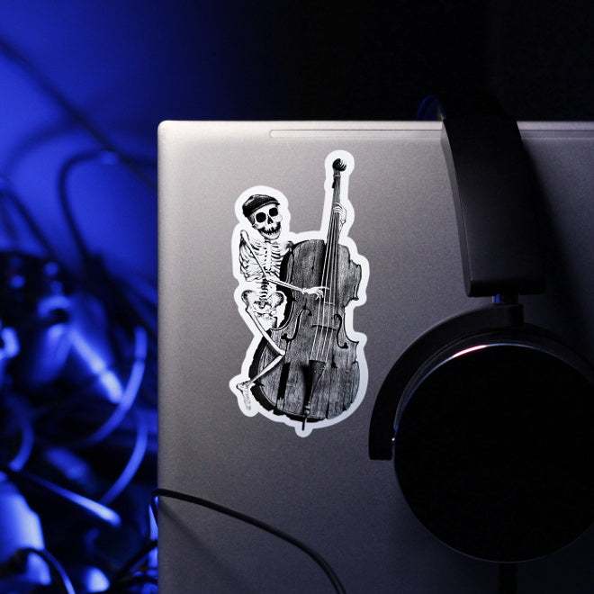 Kiszkiloszki sticker slapped on a silver laptop. A happy skeleton jazzman in a cap is playing on an old, broken double bass.
