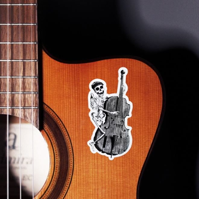 Kiszkiloszki sticker slapped on a front of a guitar. A happy skeleton jazzman in a cap is playing on an old, broken double bass.
