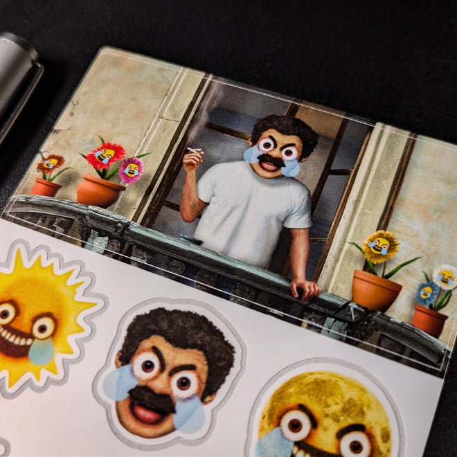 A close-up photo of a Kiszkiloszki sticker sheet placed on a table. The stickers include designs such as the AAAaaa Guy, an angry-sad man screaming on a balcony with big blue tears running down his face, as well as flowers, a sun, and a moon with similar features.
