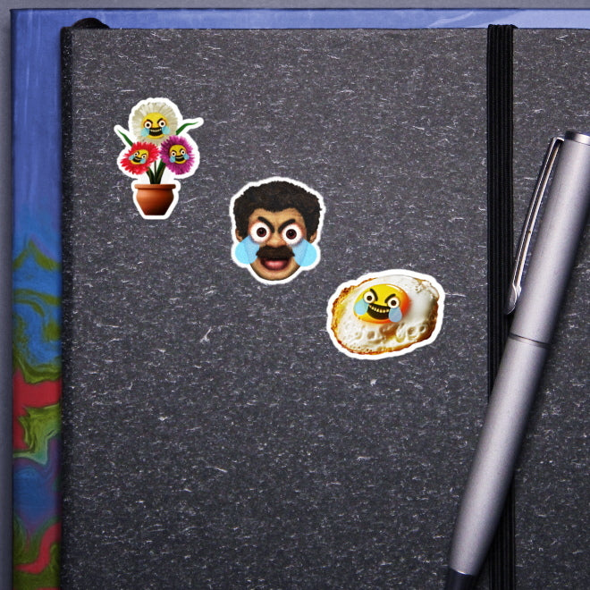 A visual showcase of Kiszkiloszki stickers on a gray notebook cover. Featured are three unique designs: angry, crying flowers in a pot; the head of a comically angry, crying man; and an angry, crying fried egg. A silver pen clipped to the notebook completes the scene.