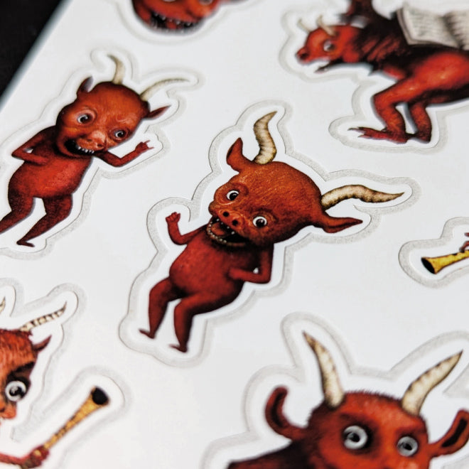 A close-up photo of a Kiszkiloszki sticker sheet. The stickers include designs such as cute little red devils dancing and playing trumpets with their butts.