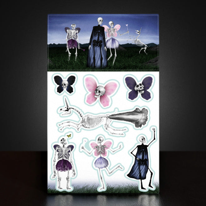 A photo of a Kiszkiloszki The Death Fairy Tales sticker sheet. The stickers include designs such as smiling skulls with butterfly wings, smiling skeleton super hero, the death fairy and a happy, flying skeletal unicorn with smoke comically jetting from its buttocks.