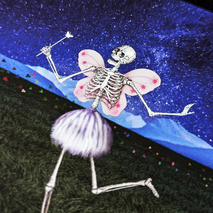 The Death Fairy. A close-up photo of an art print featuring a whimsical skeleton figure with butterfly-like pink wings and a small magical wand. The skeleton is positioned against a vibrant, starry blue background.