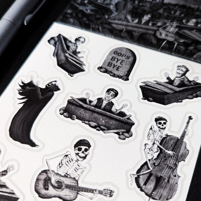 A close-up photo of a Kiszkiloszki sticker sheet. The stickers include designs such as happy peaople in their graves, dancing Death in a black robe, smiling skeletons playing music on guitar and double bass, a tombstone with "oops bye bye" sign on it.